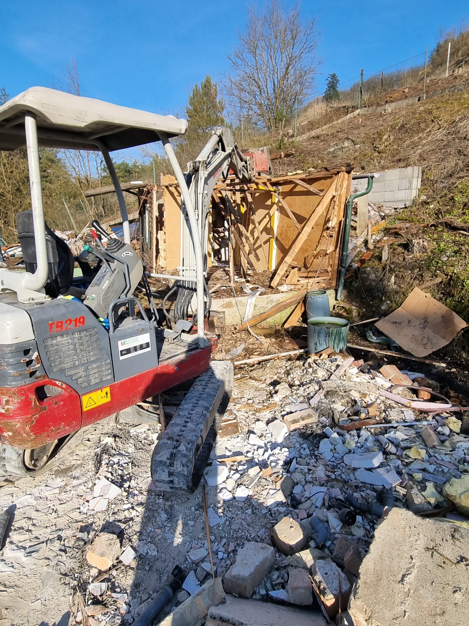 Takeuchi-Minibagger in Nahaufnahme beim Abriss eines Kleingartenhauses in Hanglage