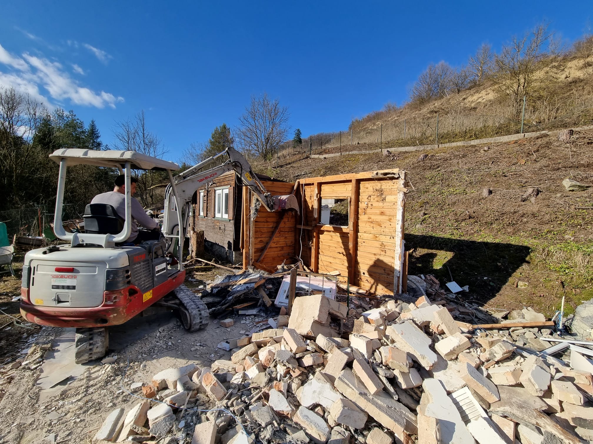 Takeuchi-Minibagger beim Kleingartenhaus-Abbruch mit Ziegel-Bauschutt im Vordergrund
