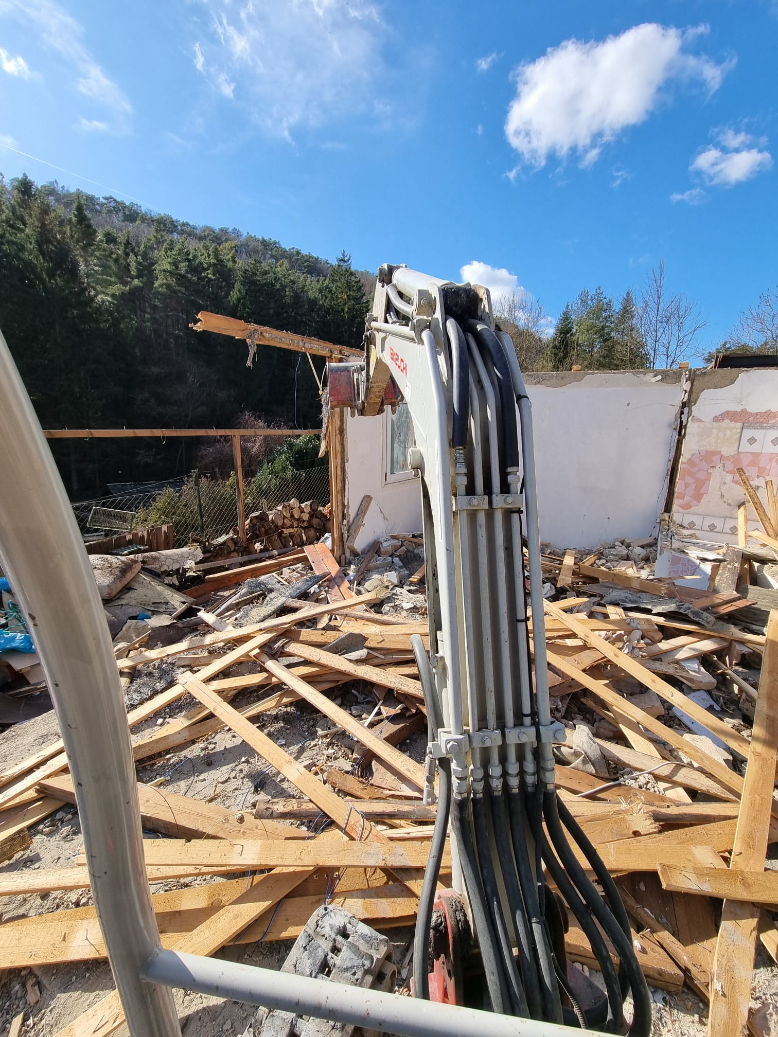 Baggerarm eines Minibaggers über den Holztrümmern eines abgerissenen Kleingartenhauses