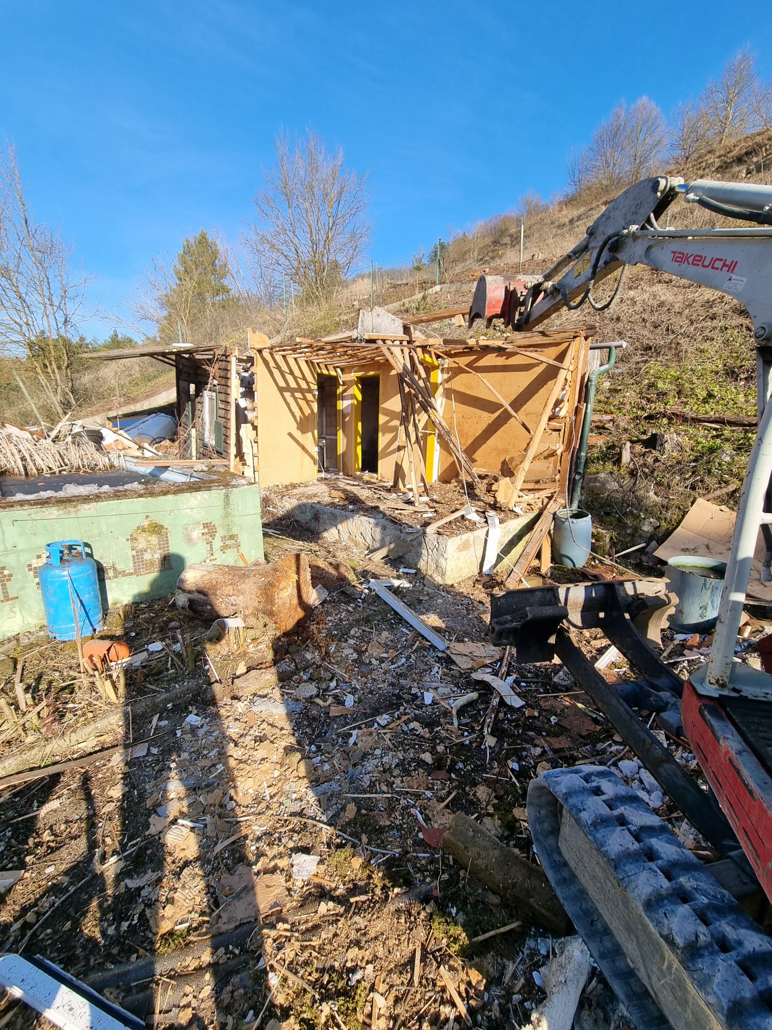 Halb abgerissenes Kleingartenhaus aus Holz mit freigelegtem Dachstuhl am Waldrand