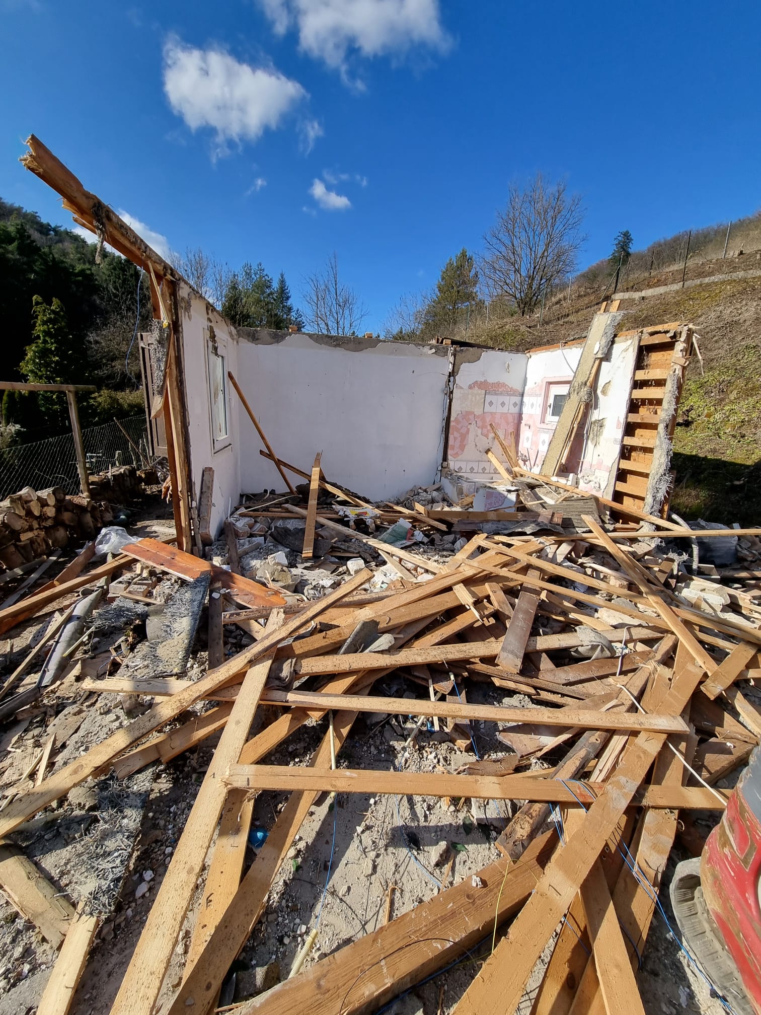 Holztrümmer eines abgerissenen Kleingartenhauses in Hanglage vor weißer Innenwand