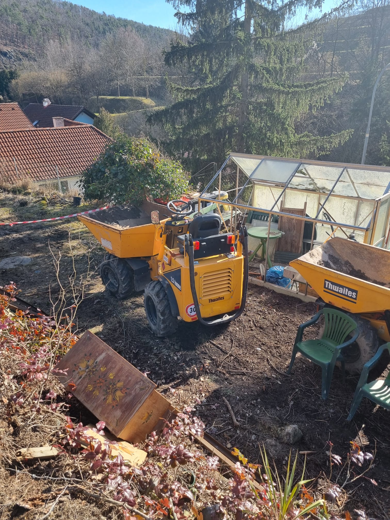 Kompakter gelber Thwaites-Minidumper und Takeuchi-Minibagger beim Kleingartenhaus-Abriss im Garten