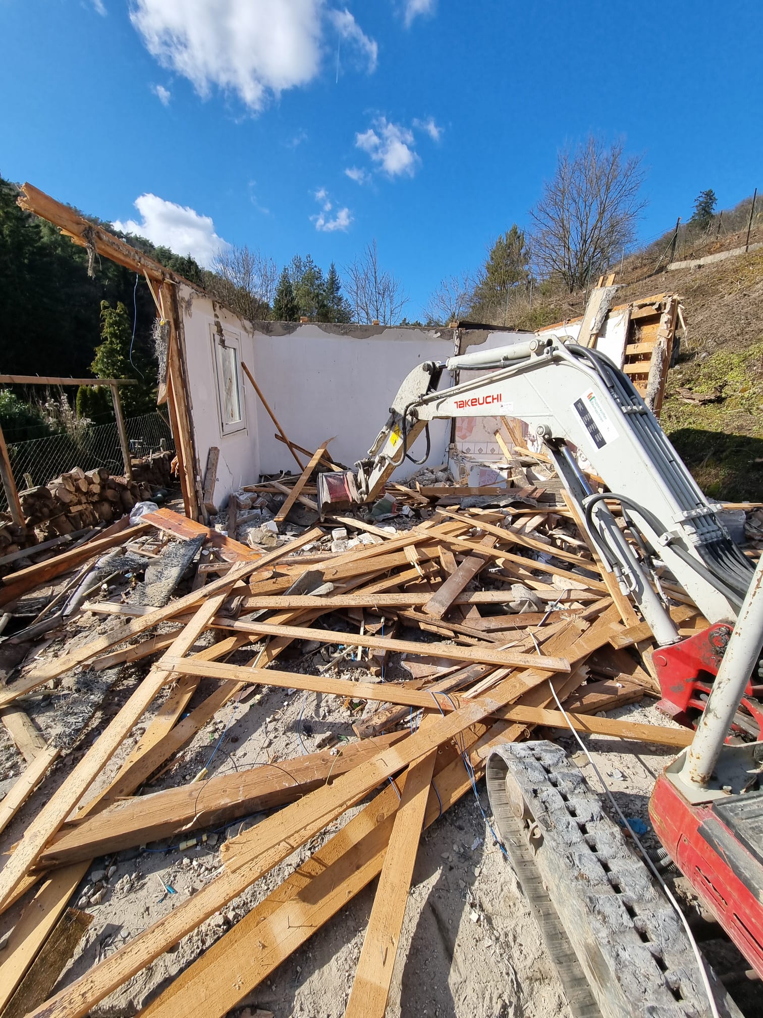 Takeuchi-Minibagger reißt das Dach eines Kleingartenhauses in Hanglage ab