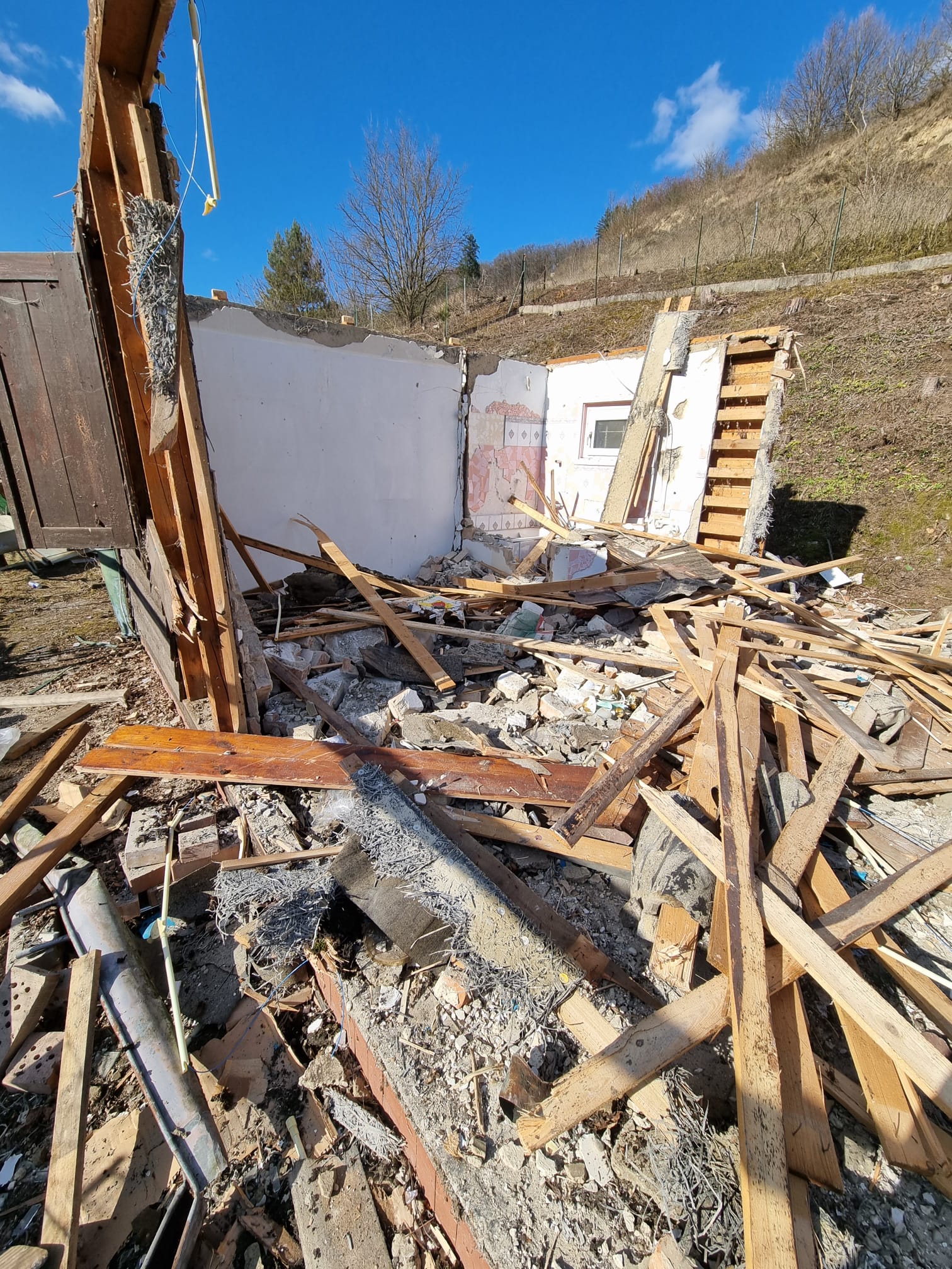 Stehen gebliebene weiße Innenwand inmitten der Holztrümmer eines abgerissenen Kleingartenhauses